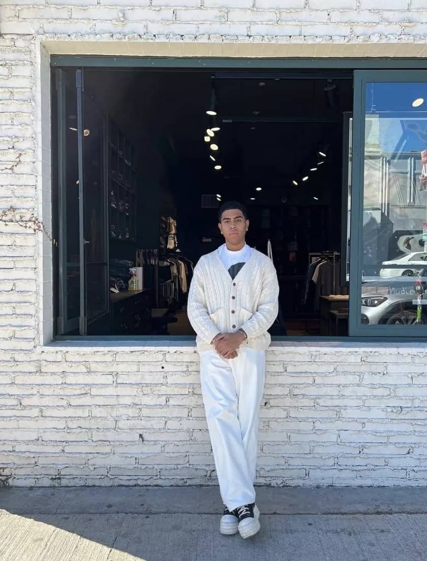 man wearing all white leaning against a white brick wall with a big open window