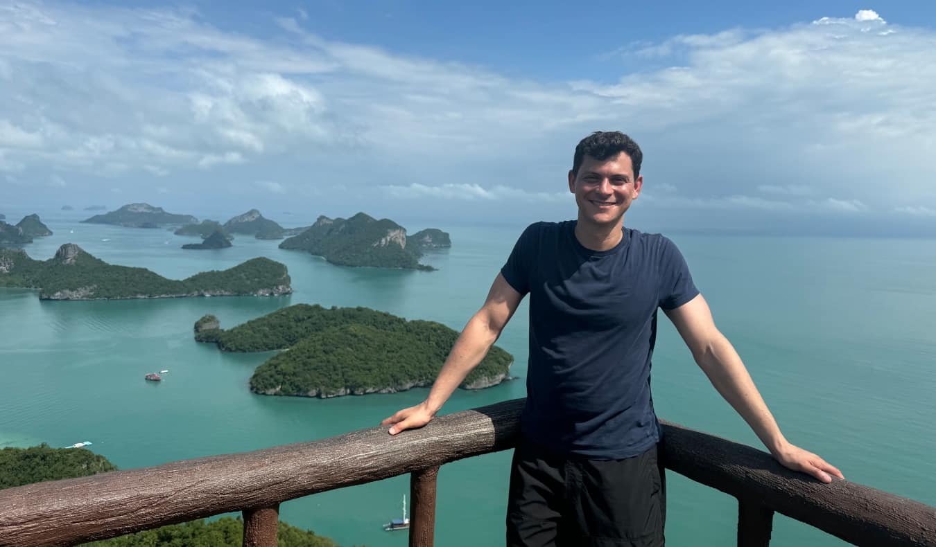 Nomadic Matt in Thailand, smiling and looking at the camera at a scenic overlook, with turquoise water peppered with lush islands behind him